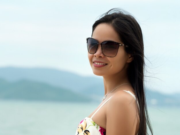 Retrato de joven bella mujer asiática con gafas de sol y de pie en la playa. Concepto de verano, relajación o vacaciones.