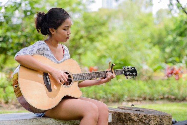 Retrato de joven bella mujer asiática tocando la guitarra en el parque al aire libre