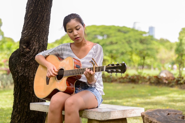 Retrato de joven bella mujer asiática tocando la guitarra en el parque al aire libre