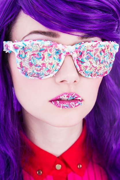 Retrato de joven bella mujer con cabello morado y gafas cubiertos por coloridos caramelos de azúcar