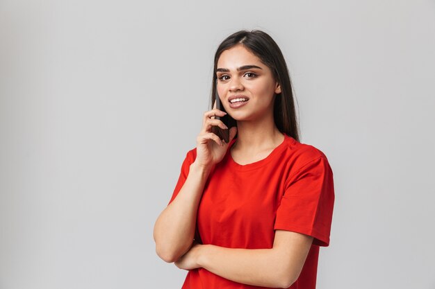 Retrato de una joven y bella mujer casualy vestida de pie aislado en blanco, hablando por teléfono móvil