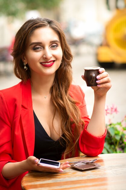 Retrato de una joven y bella mujer caucásica sonriente sentada en la mesa con una taza de café en un café al aire libre