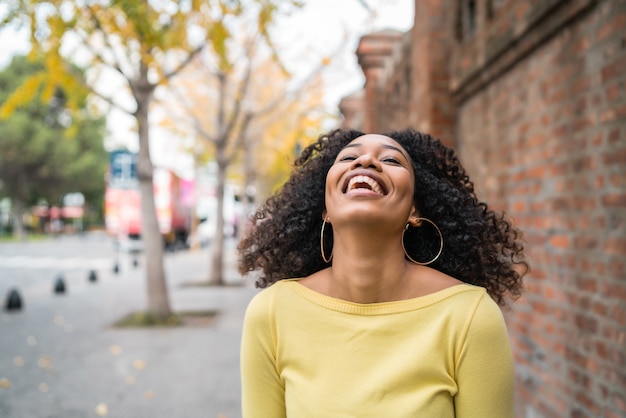 Retrato de joven y bella mujer confiada afroamericana riendo en la calle. Al aire libre.