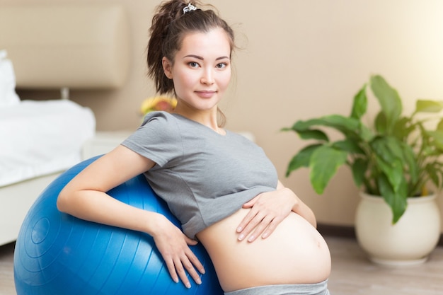 Retrato de una joven y bella mujer embarazada ejercicios con fitball azul en la sala doméstica. Ejercicio y fitness, concepto de embarazo.