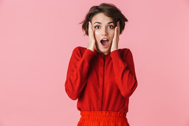 Retrato de una joven y bella mujer emocionada vistiendo ropa roja que se encuentran aisladas sobre fondo de color rosa