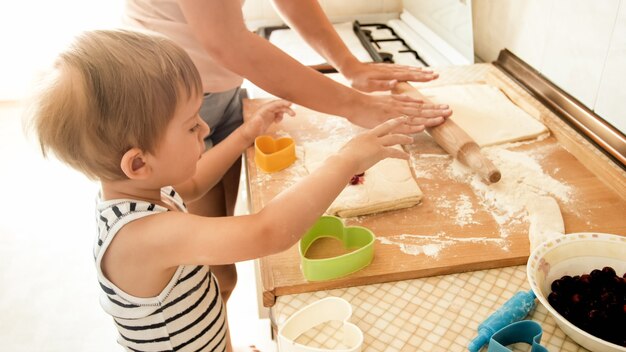 Retrato de joven bella mujer enseñando a su pequeño niño haciendo galletas y horneando pasteles en la cocina de casa