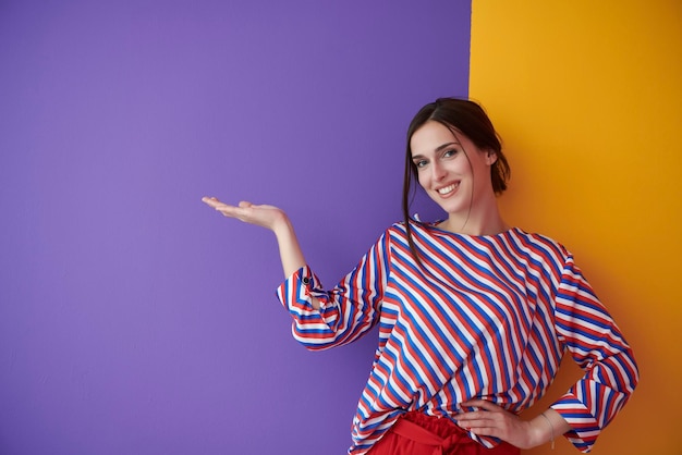 Retrato de una joven y bella mujer feliz y sonriente en un gesto de presentación con la palma abierta aislada en un fondo morado y amarillo. Modelo femenino en ropa de moda moderna posando en el estudio