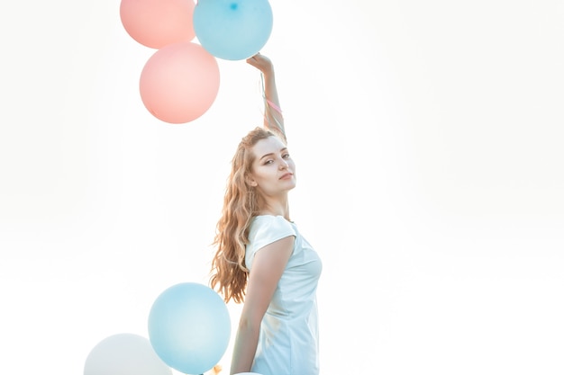 Retrato de joven bella mujer con globos multicolores volando contra el cielo