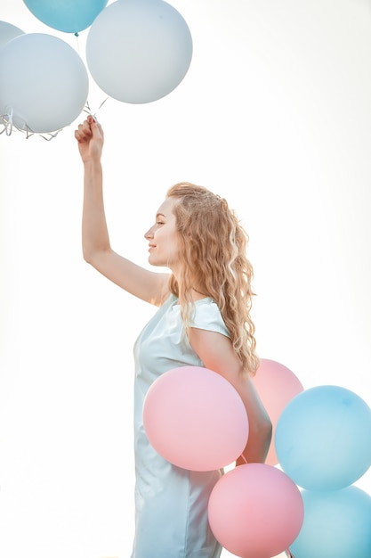 Retrato de joven bella mujer con globos multicolores volando contra el cielo