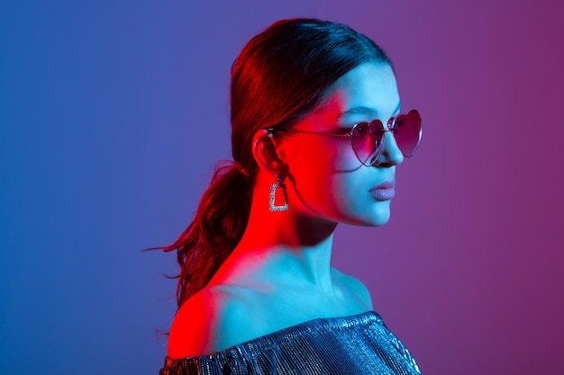 Retrato de una joven y bella mujer con iluminación de colores en gafas de sol