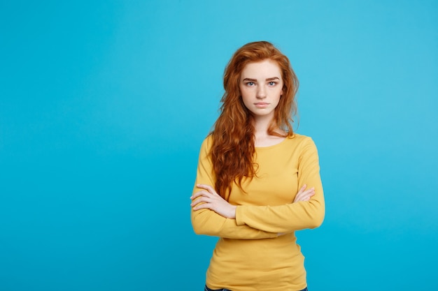 Retrato de joven bella mujer de jengibre con tierna cara seria cruzando los brazos aislados en el espacio de copia de pared azul pastel