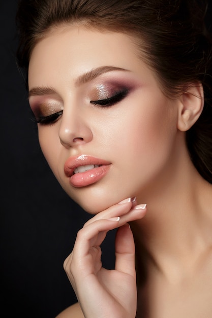 Retrato de joven bella mujer con maquillaje de noche tocando su rostro sobre fondo negro