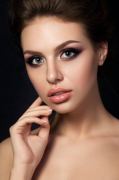 Foto retrato de joven bella mujer con maquillaje de noche tocando su rostro sobre fondo negro