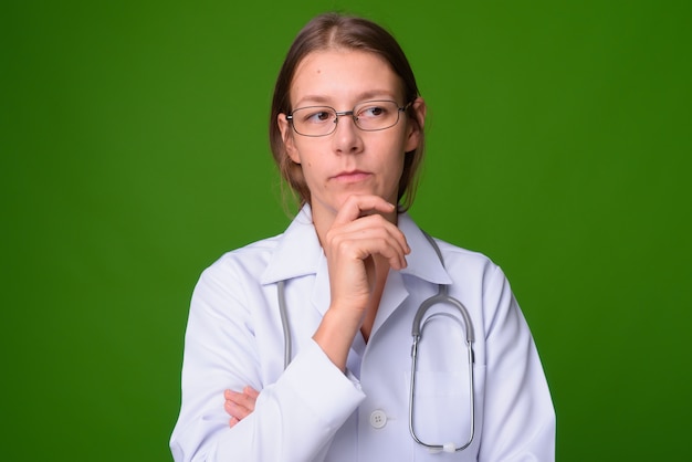 Retrato de joven bella mujer médico contra la pared verde