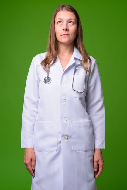 Retrato de joven bella mujer médico contra la pared verde