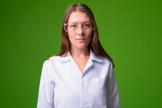 Retrato de joven bella mujer médico contra la pared verde