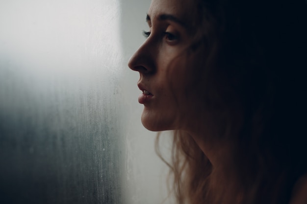 Retrato de joven bella mujer de perfil junto a la ventana empañada