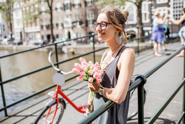 Retrato de una joven y bella mujer de pie con bouguet de tulipanes rosas en el puente en la ciudad vieja de Amsterdam