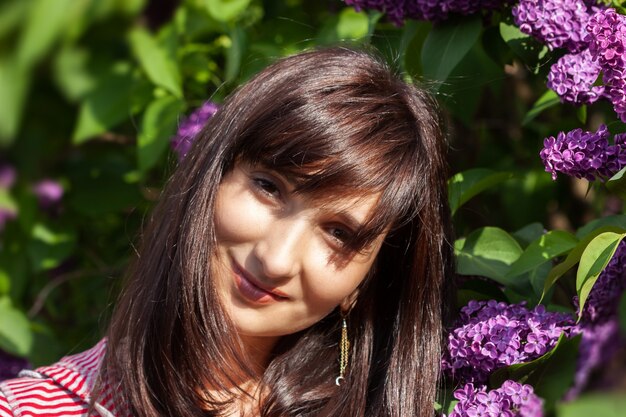 Retrato de una joven y bella mujer posando entre lilas florecientes. Mujer entre arbustos de lilas florecientes en primavera.