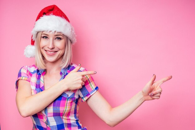 Retrato de joven bella mujer rubia asombrada con caja de regalo de Navidad sobre fondo rojo. dama con una camisa a cuadros y santa claus sostienen una bolsa llena de regalos sobre un fondo rosa en el estudio.