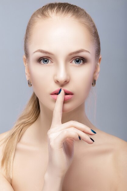 Retrato de una joven y bella mujer rubia con ojos azules en primer plano de fondo gris. mujer haciendo un gesto tranquilo