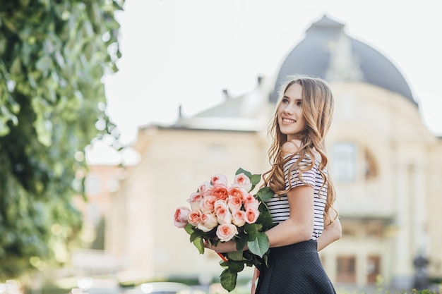 Retrato de una joven y bella mujer rubia de pie con un ramo de rosas