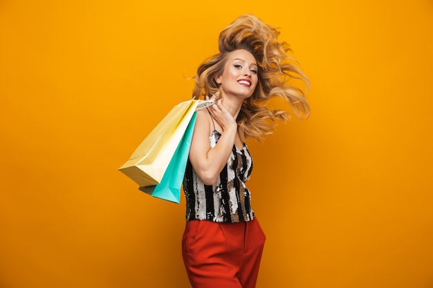 Retrato de una joven y bella mujer rubia que se encuentran aisladas sobre fondo amarillo, llevando bolsas de la compra.