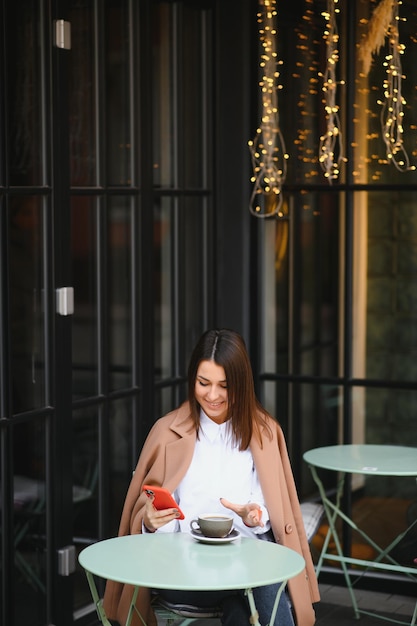 Retrato de joven bella mujer sentada en un café bebiendo café al aire libre