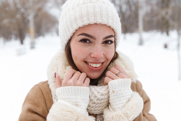 retrato de una joven y bella mujer con sombrero y bufanda caminando al aire libre en la nieve del invierno.
