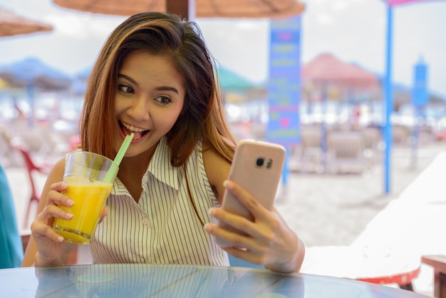 Retrato de joven bella mujer turista asiática sentada en el restaurante junto a la playa al aire libre