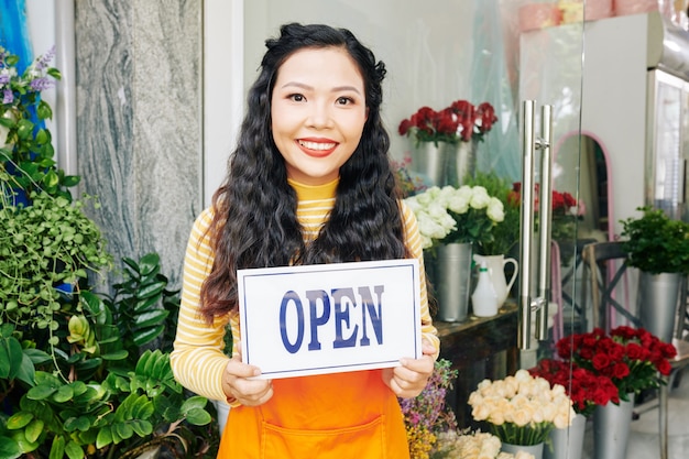 Retrato de joven y bella mujer vietnamita en floristería con cartel abierto