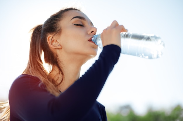 Retrato de joven bella mujer vistiendo ropa deportiva azul agua potable en el parque