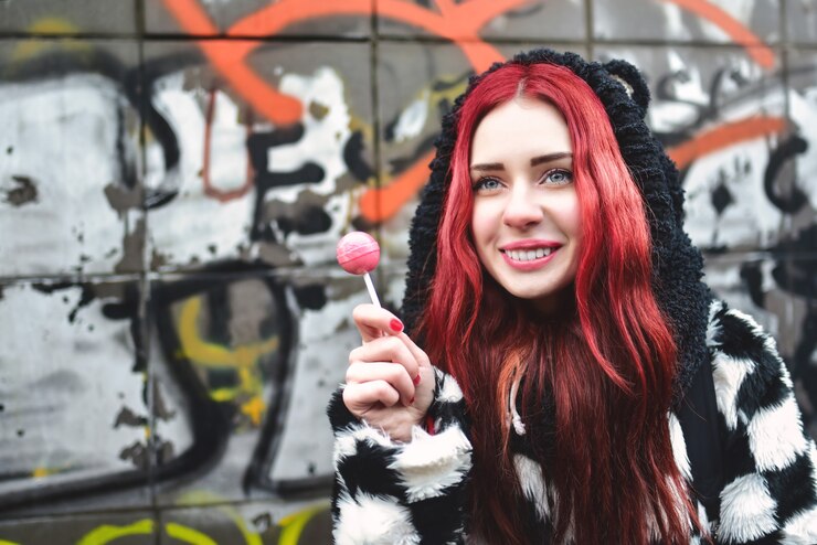 Foto retrato de una joven belleza adolescente en una sudadera con capucha con una deliciosa piruleta rosa, posando contra una pared de graffiti.