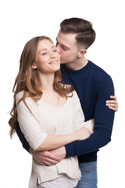 Retrato de joven besando a su novia mientras la abraza. Niña sonriendo con los ojos cerrados.