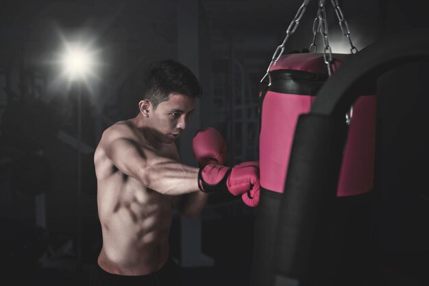 Retrato de un joven boxeador asiático golpeando un saco de boxeo en el gimnasio