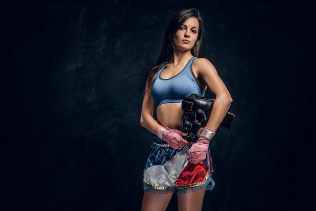 Retrato de una joven boxeadora con su casco en las manos en un estudio fotográfico oscuro.