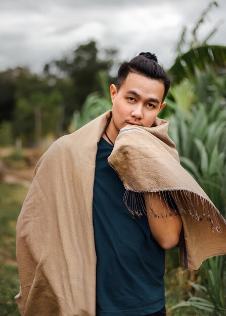 Foto retrato de un joven con una bufanda de pie contra las plantas