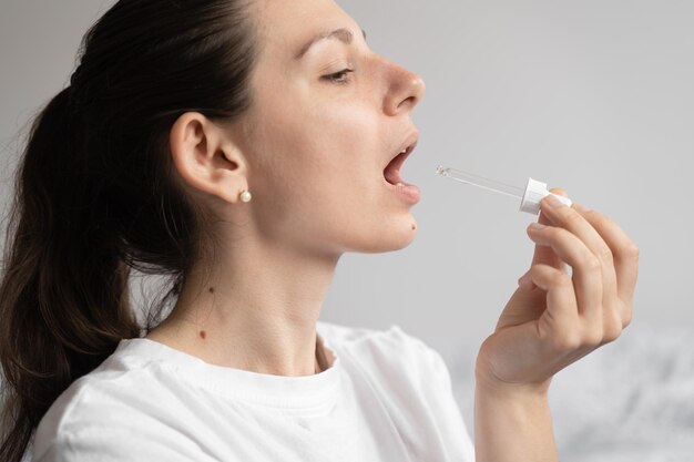 Retrato de una joven de cabello oscuro que toma un suplemento de aceite con un cuentagotas de vidrio Aceite de medicina de cáñamo CBD que se aplica en la lengua