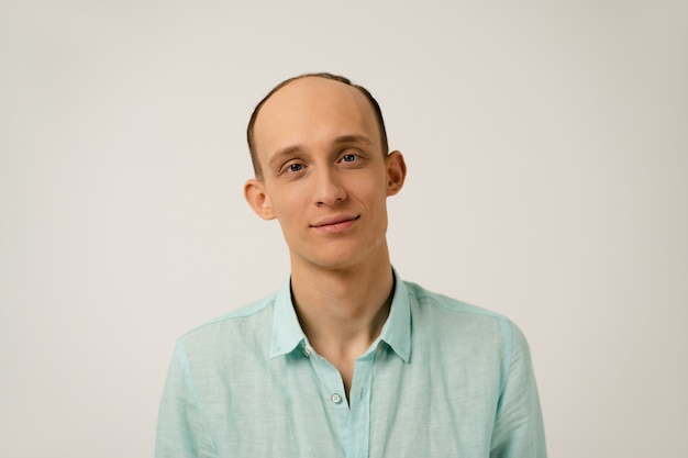 Retrato de joven calvo con divertidas orejas que sobresalen en camisa azul coral con mirando al frente aislado sobre una pared blanca en estudio