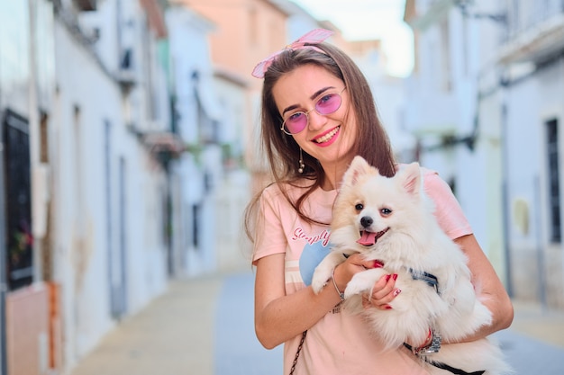 Retrato de una joven caminando con un pomerania esponjoso blanco.