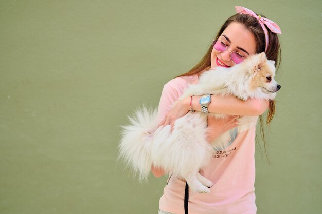 Retrato de una joven caminando con un pomerania esponjoso blanco.