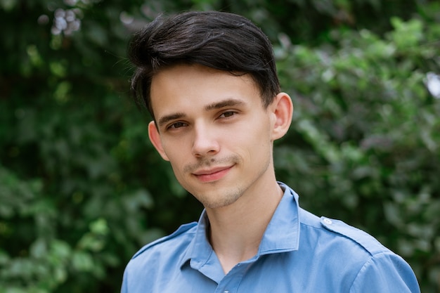 Retrato de un joven con una camisa azul sobre un verde natural sonriendo