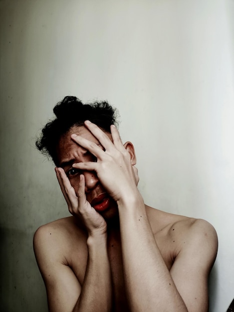 Foto retrato de un joven sin camisa cubriendo la cara contra la pared