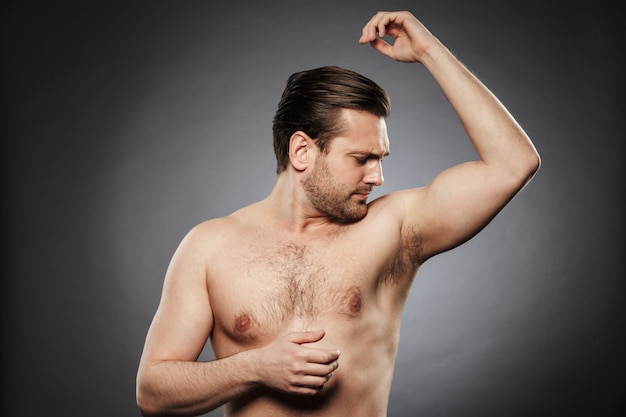 Foto retrato de un joven sin camisa que huele su axila