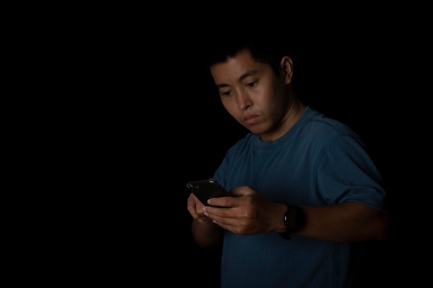 Retrato de un joven con camiseta azul usando un teléfono inteligente en un espacio de copia de fondo negro