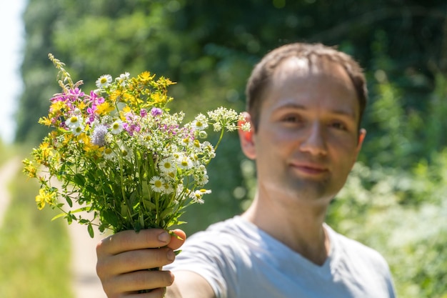 Retrato de un joven con una camiseta blanca y un ramo de flores en las manos Un chico posa en el fondo de un campo de flores y un camino de tierra en el pueblo La cara de una persona feliz