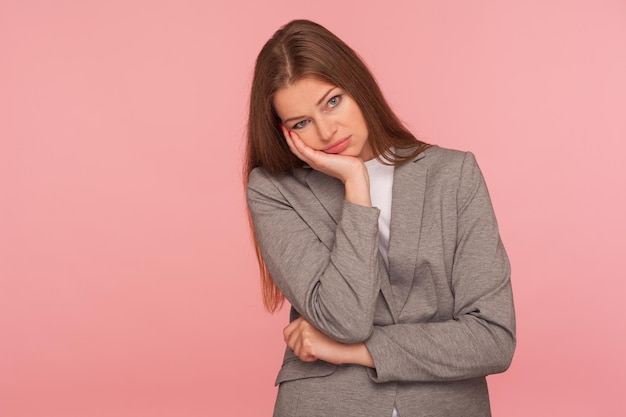 Retrato de una joven cansada y aburrida con traje de negocios escuchando una historia tediosa con una expresión sombría y deprimida, siendo indiferente a la conversación, falta de ideas. tiro del estudio aislado sobre fondo de color rosa