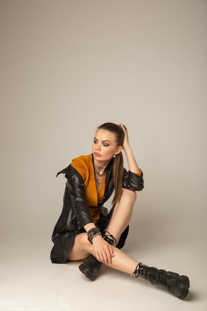 Retrato de una joven caucásica atractiva posando con una chaqueta de cuero, sentada en un suelo blanco en un estudio blanco. Pruebas de modelo de niña bonita en ciclorama.