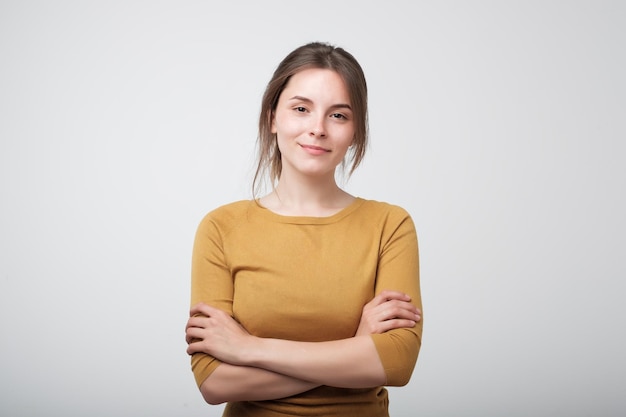 Retrato de una joven caucásica con camisa amarilla parada casualmente cerca de una pared gris