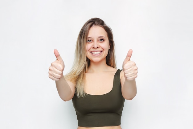 Foto retrato de una joven caucásica feliz sonriente exitosa mujer rubia en un top verde mostrando los pulgares para arriba